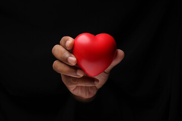 Asian male dark skinned single hand fist finger on black background holding red rubber hart love...