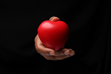 Asian male dark skinned single hand fist finger on black background holding red rubber hart love shape