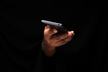 Asian male dark skinned single hand fist finger on black background holding using smart phone cell...