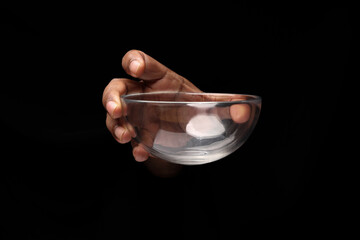 Asian male dark skinned single hand fist finger on black background holding small transparent glass bowl