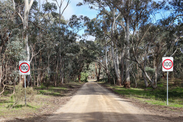 dirt road through bushland with speed signs 100 kmh