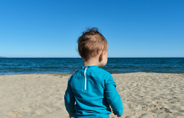 unrecognizable little boy on the beach wearing a sun protection t-shirt (upf ), to protect the skin...