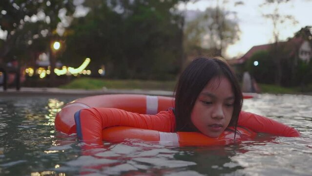 Depressed Asian girl is floating on water in a swimming pool with sad expression.