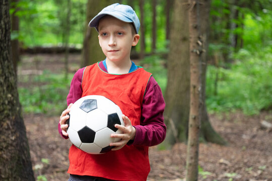 Young boy in red shirt and denim cap holds his hands football. Sport and childhood concept