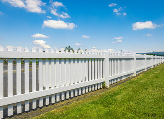 Fototapeta na wymiar White wooden fence on the blue sky background. Green lawn and wooden white fence on sunny summer day