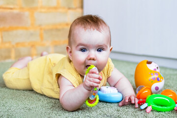 Cute little baby girl lying on a floor and playing with colorful plastic and wooden toys. Develop of child motor skills.