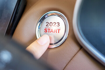 Finger press a car ignition button with 2023 START text inside  automobile. New Year New You, forecast, resolution, motivation, change, goal, vision, innovation and planning concept
