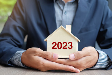 Businessman hands holding wooden House model with 2023 New Year text. Property insurance and real...