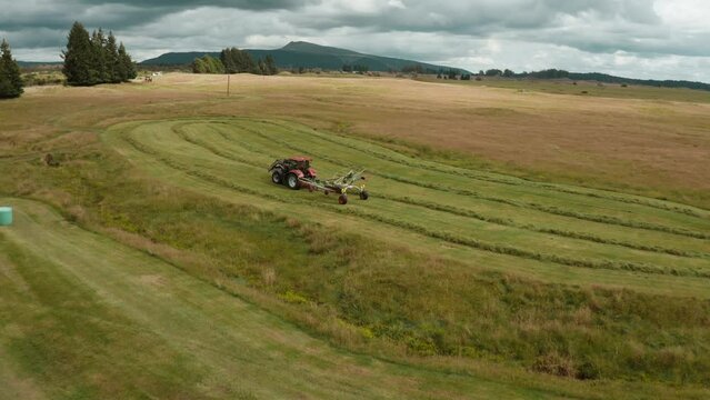 Tractor using mounted hay raking machine in preparation for baling, rotary tedder
