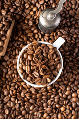 Roasted coffee beans and star anise in a mug on a background of coffee beans.