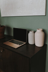 Laptop computer and clay pots on retro wooden cabinet table against green wall
