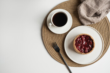 Morning breakfast with coffee and berry pie. Aesthetic still life composition with dessert, coffee, flowers bouquet, linen blanket, fork on white table. Flat lay, top view