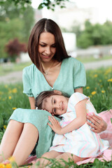 Portrait of a happy mother and daughter resting on the grass on a summer day.Family and summer concept.