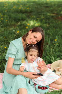 Caucasian mother and daughter kid use a smartphone in the park on a summer day.Mom and child talk on video call,make self-portrait picture together.Summer, technology,social media,family concept.