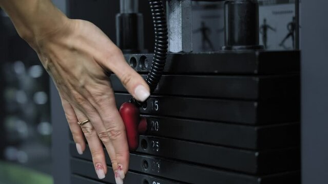 Female hand changes weight of stack plates at sports equipment. Sport concept. Close-up in 4K, UHD