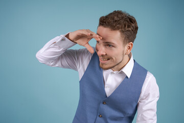 Suspicious young man in white shirt in suit, holding his hand near his eyes to see better in the...