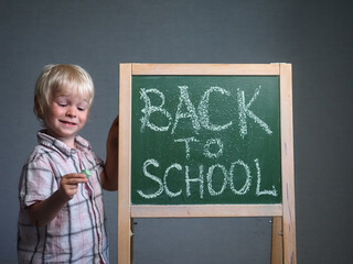 Back to school. The blonde boy write a chalk inscription on the board. Schoolboy from primary school. Happy pupil 