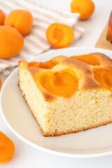 Soft homemade pie with fresh apricots. Square slice of yeast fruit cake on dish.