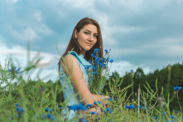 Obraz na płótnie Canvas Young pretty woman among the field of beautiful cornflowers