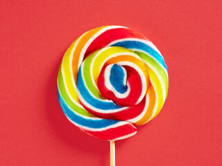 Rainbow colored swirl round candy lollipop on red background. Close up macro.