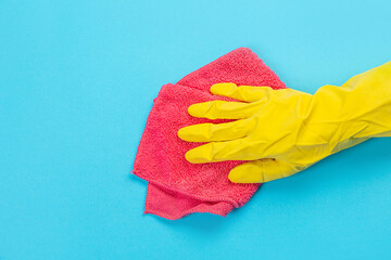 a female hand in a yellow rubber protective glove with a micro fiber red rag wiping a blue wall from dust. A maid or housewife takes care of the house. Spring general or regular cleaning. 