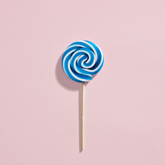Blue and white colored swirl round candy lollipop on pink background.