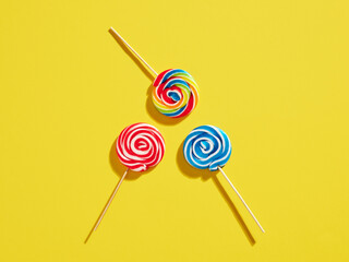 Colorful swirl round candy lollipops on yellow background.