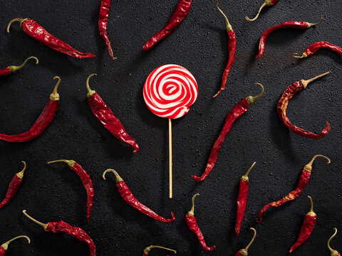 Red and white colored swirl round candy lollipop with dry red hot chili peppers. Sweet and hot food contrast.