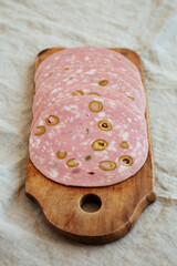 Organic Sliced Mortadella Sausage with Olives on a rustic wooden board, side view.