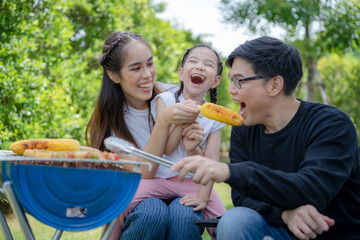 Asian family laughs and smiles as they eat barbecue in courtyard to house. A bright cute daughter...