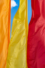 Multi-colored holiday flags flutter in the wind against a blue sky - yellow, orange, red