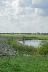 Hilly green shore of a village lake under a blue cloudy sky on a summer day, without people