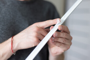 Man putting glue by finger on decorative plastic corner for the wall protection in apartment. 