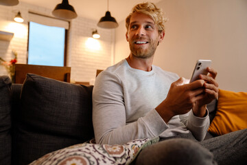 Blonde bearded man using mobile phone while sitting on sofa