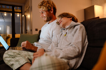 Ginger man using laptop while resting with his son on couch