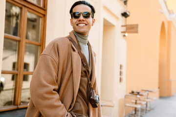 Young man wearing coat and sunglasses laughing while walking on street