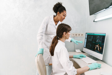 Multiracial dentists examining x-ray while working with computer