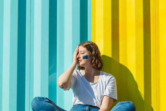 Teenage girl with European Union paint on face covering eye in front of blue and yellow wall
