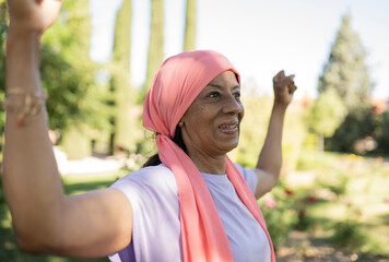 Cheerful elderly woman with arms raised in park