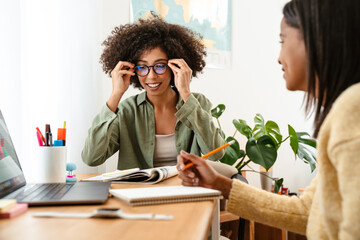 Black girl writing in exercise book while doing homework with her mother
