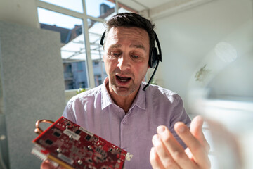 Customer service representative talking on headset looking at machine part in office