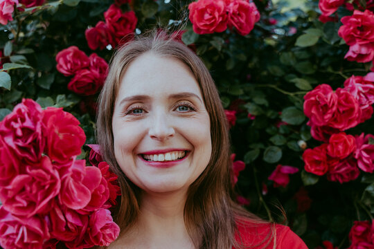 Happy Woman Amidst Plant Of Red Roses