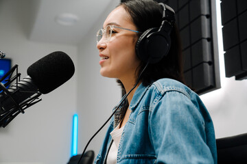 Beautiful happy young female radio host broadcasting in studio