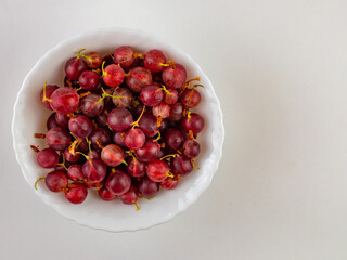 Fresh, sweet red gooseberries in a white cup on a white background.