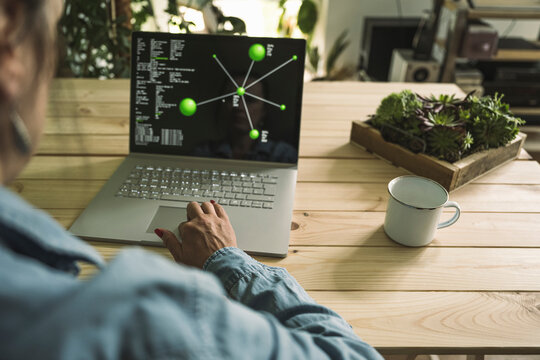 Businesswoman working with laptop by coffee cup and plant on table at home office