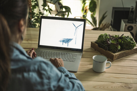 Freelancer with sketch of solar panel and wind turbine on laptop screen at home office