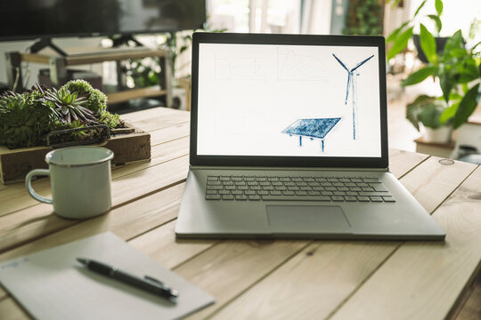Solar panel and wind turbine on screen of laptop at home