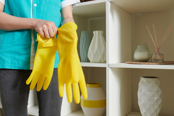 Close-up of cleaner girl putting on yellow rubber gloves before cleaning the room