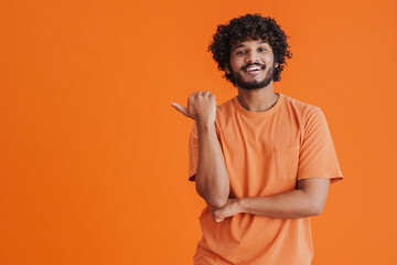 Young indian handsome curly smiling man pointing left with thumb