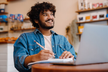 Young indian smiling handsome man studying with laptop at cafe